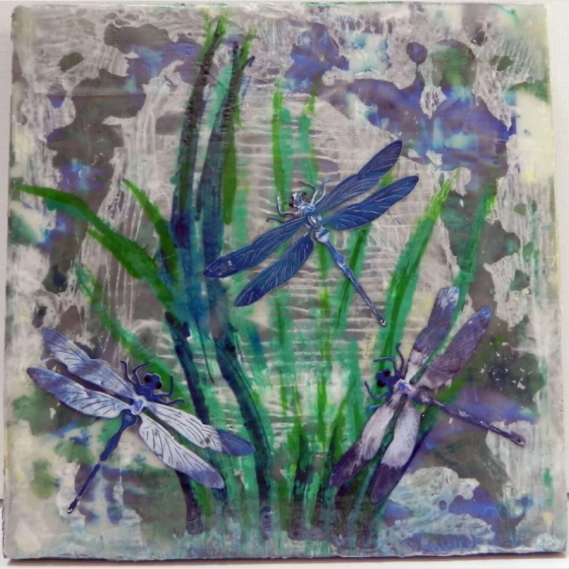 Artistic painting of three blue dragonflies among green grass and blue flowers.